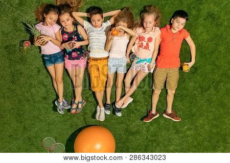 Group Of Happy Children Playing Outdoors. Kids Having Fun In Spring Park. Friends Lying On Green Gra