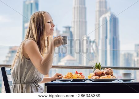 A Young Woman Is Having Breakfast On The Balcony. Breakfast Table With Coffee Fruit And Bread Croisa