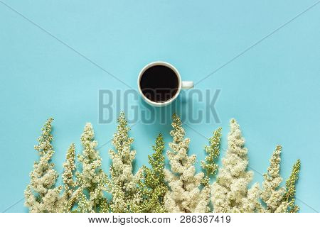 Cup Of Coffee And Row Blooming Twig White Flowers On Blue Paper Background Flat Lay Top View Concept