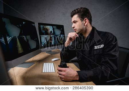 Concentarted Guard Looking At Computer Monitor And Holding Walkie-talkie