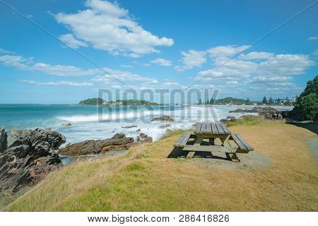 Outdoor Table Beside Walking Track With Distant Waves Smoothed By Long Exposure Washing In Around Ro