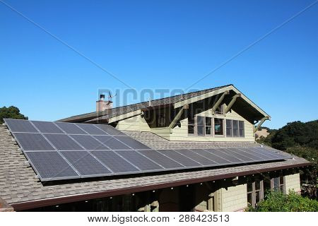 Solar Panels On Roof Of House. Horizontal Orientation, Blue Sky, Gray Panels On Brown Roof.