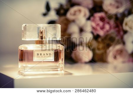 Perfume Bottle On Table And Flowers At Background. Aromatic Eau De Toilette. A Beautiful Perfume Bot