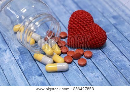 Pills And Red Knitted Heart On Blue Wooden Table. Concept Of  Hypertension, Health Care, Treatment O