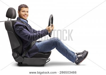 Full length profile shot of a young man in a car seat with a fastened seat belt holding a streering wheel isolated on white background