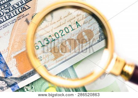 Hundred Dollar Under A Magnifying Glass On The Bacdrop Euro  Banknote. Сoncept Of The Main Internati