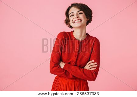 Portrait of a happy young woman wearing red clothes standing isolated over pink background