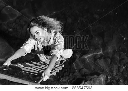 Ambition Wings Her Spirit. Sexy Woman Climbing Up Rope Ladder. Sensual Woman Hang On Rope Over Water