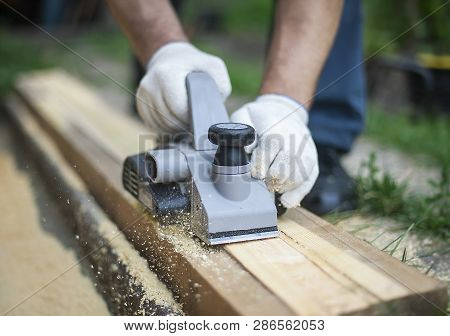 The Hand Of A Man Working With Electric Planers Outdoor. Shavings Debris Ejected From The Machine. H