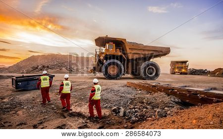 Large Dump Trucks Transporting Platinum Ore For Processing With Mining Safety Inspectors In The Fore