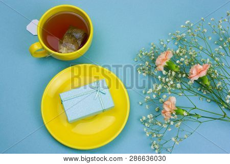 Top View Tea Cup With Tea Bag,gift Box On A Plate And Bouquet Of Flowers On A Pastel Blue Background