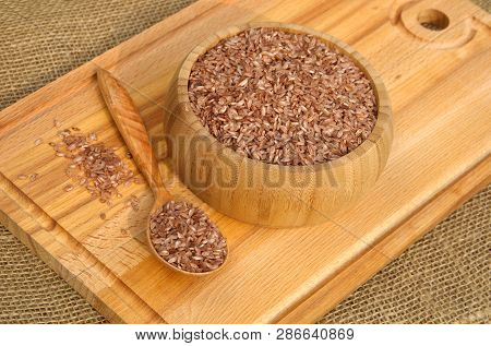 Uzbek Devzira, The Red Rice In A Bamboo Bowl And A Wooden Spoon On A Cutting Board