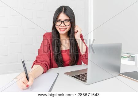 Young Attractive Asian Businesswoman, Long Black Hair, Wearing Glasses, Smiling, Writing Note On Not