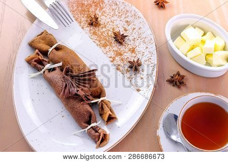 Chocolate Russian Pancakes, Blini With Curd Filling On The Plate. Served With A Cup Of Tea And Butte