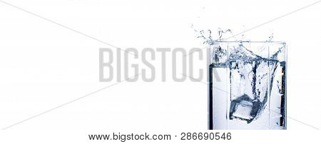 Splash Of Water In A Glass From An Ice Cube On A White Background. Concept Of Quenching Thirst And C