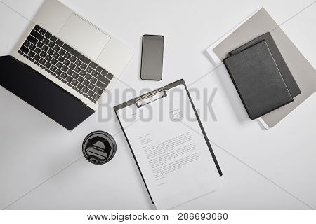 Top View Of Documet On Clipboard, Paper Cup, Laptop, Smartphone, Notebooks And Folder