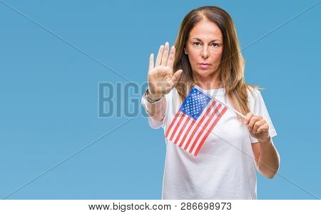 Middle age hispanic woman holding flag of United States of America over isolated background with open hand doing stop sign with serious and confident expression, defense gesture