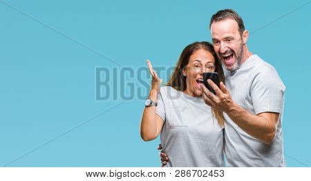Middle age hispanic couple texting message on smartphone ver isolated background very happy and excited, winner expression celebrating victory screaming with big smile and raised hands