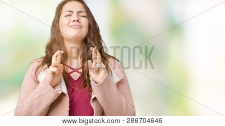 Beautiful plus size young woman wearing winter coat over isolated background smiling crossing fingers with hope and eyes closed. Luck and superstitious concept.