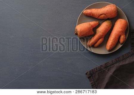 Misshapen Ugly Fresh Carrots With Imperfections And Splits On A Plate Viewed From Overhead On Grey W