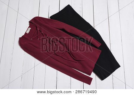Clothes And Accessories. Black Midi Skirt And Red Sweater With Lacing On White Wooden Floor Planks. 