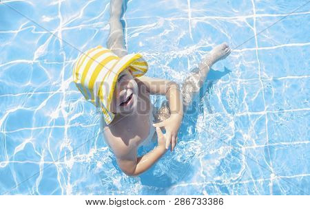 3 Years Toddler Boy Enjoying Swimming Pool At Shallow Area. He Wears Yellow Stripped Hat