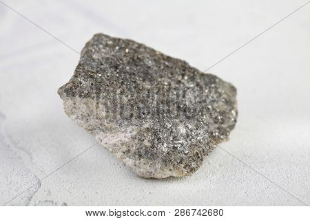Natural Mineral Rock Specimen - Raw Arsenopyrite Stone On White Cement Background From Kachkarskoe, 