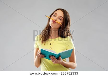 education, school, inspiration and people concept - young woman or teenage student girl in yellow t-shirt with diary or notebook and pencil-mustache over grey background