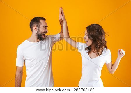 Image of young people man and woman in basic clothing slapping their hands together while standing isolated over yellow background