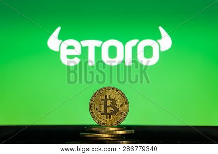 Bitcoin On A Stack Of Coins With Etoro Logo On A Laptop Screen. Cryptocurrency And Blockchain Adopti