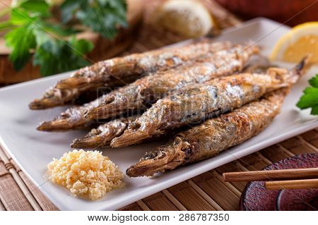 A Plate Of Delicious Grilled Shishamo With Roe And Lemon And Parsley Garnish.