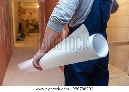 Worker Is Holding The White Wallpaper Roll Before Gluing In Apartment Is Inder Construction, Remodel