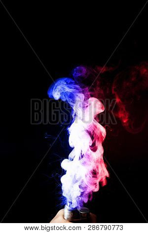 Male Hand Holds Vape. Vape Clouds Splash From Vape Coil On Black Background. Fog Is Dual Color -- Bl