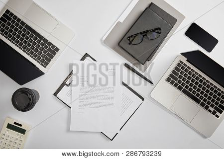 Top View Of Documet On Clipboard, Paper Cup, Laptops, Smartphone, Notebooks, Folder, Calculator And 