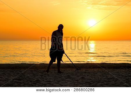 Man Silhouette With Metal Detector On The Beach In Sun Set