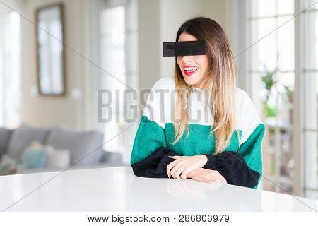 Young beautiful woman blindfold eyes with black censor band at home looking away to side with smile on face, natural expression. Laughing confident.