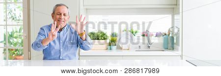 Wide angle perspective of handsome senior man at home showing and pointing up with fingers number eight while smiling confident and happy.