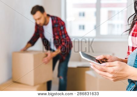 Selective Focus Of Woman Holding Smarthone Near Man With Box On Background