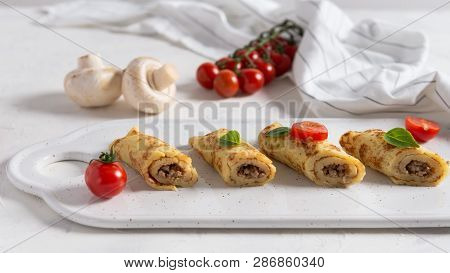 Savory Crepe Rolls With Meat Filling Served With Fresh Basil And Cherry Tomatoes. Traditional Russia