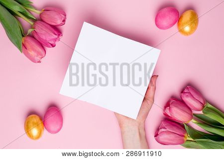 Female Hand Hold Present Card On A Pink Background With Flowers And Easter Eggs