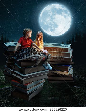 Little Girl And Boy Sitting On The Tower Made Of Big Books. Childhood Dreams, Creative And Education