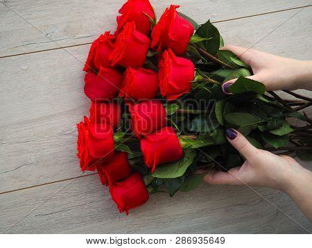 Preparing A Gift, On A Wooden Table, With Roses. Female Hand Holding A Gift, Wrapped With Ribbon, On