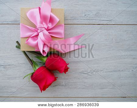 Preparing A Gift, On A Wooden Table, With Roses. Female Hand Holding A Gift, Wrapped With Ribbon, On