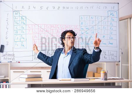 Young male chemistry teacher in front of periodic table 