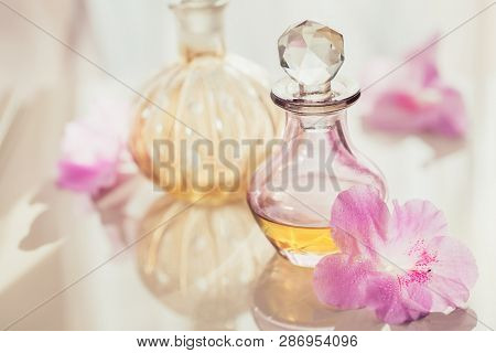 Spa Still Life With Perfume And Aromatic Oils Bottles Surrounded By Flowers, On Light Background