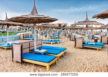 A Lot Of Chaise Lounges With Blue Mattresses On A Luxurious Beach. Umbrellas For Protection From The