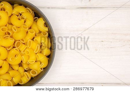 Closeup Of Lot Of Whole Raw Pasta Pipe Rigate Variety In A Grey Ceramic Bowl Flatlay On White Wood
