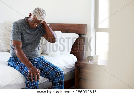 Senior Man Suffering With Neck Pain Sitting On Side Of Bed At Home