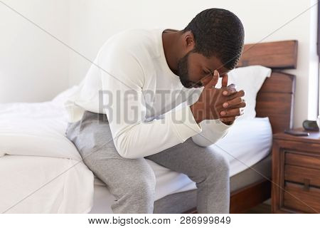 Depressed Man Looking Unhappy Sitting On Side Of Bed At Home With Head In Hands