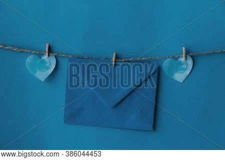 One Blue Envelope Hanging On Rope Isolated Blue Background With Two Blue Hearts On The Sides. Write 